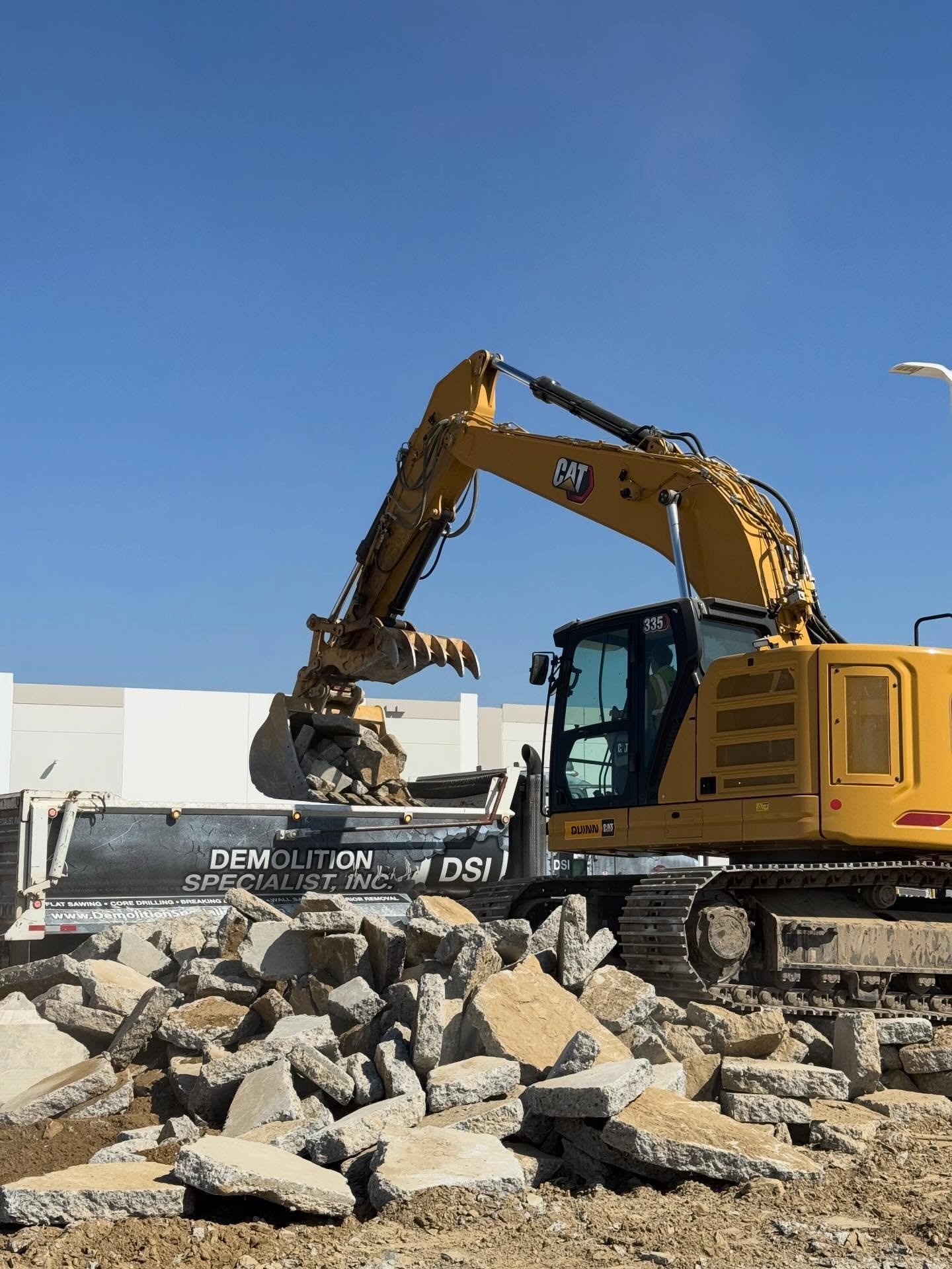 CAT 335 excavator actively loading broken concrete rubble into DSI Demolition Specialist dump truck