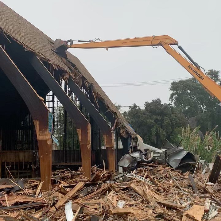 Hyundai long-reach excavator pulling apart A-frame roof structure during full building demolition