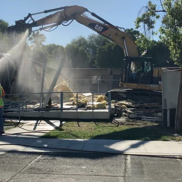 CAT excavator demolishing commercial building with water suppression spray active