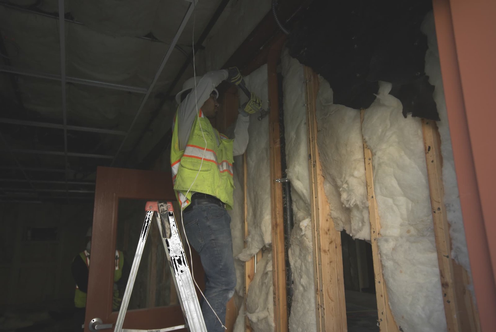 DSI worker on ladder actively dismantling wall framing and insulation during interior demolition