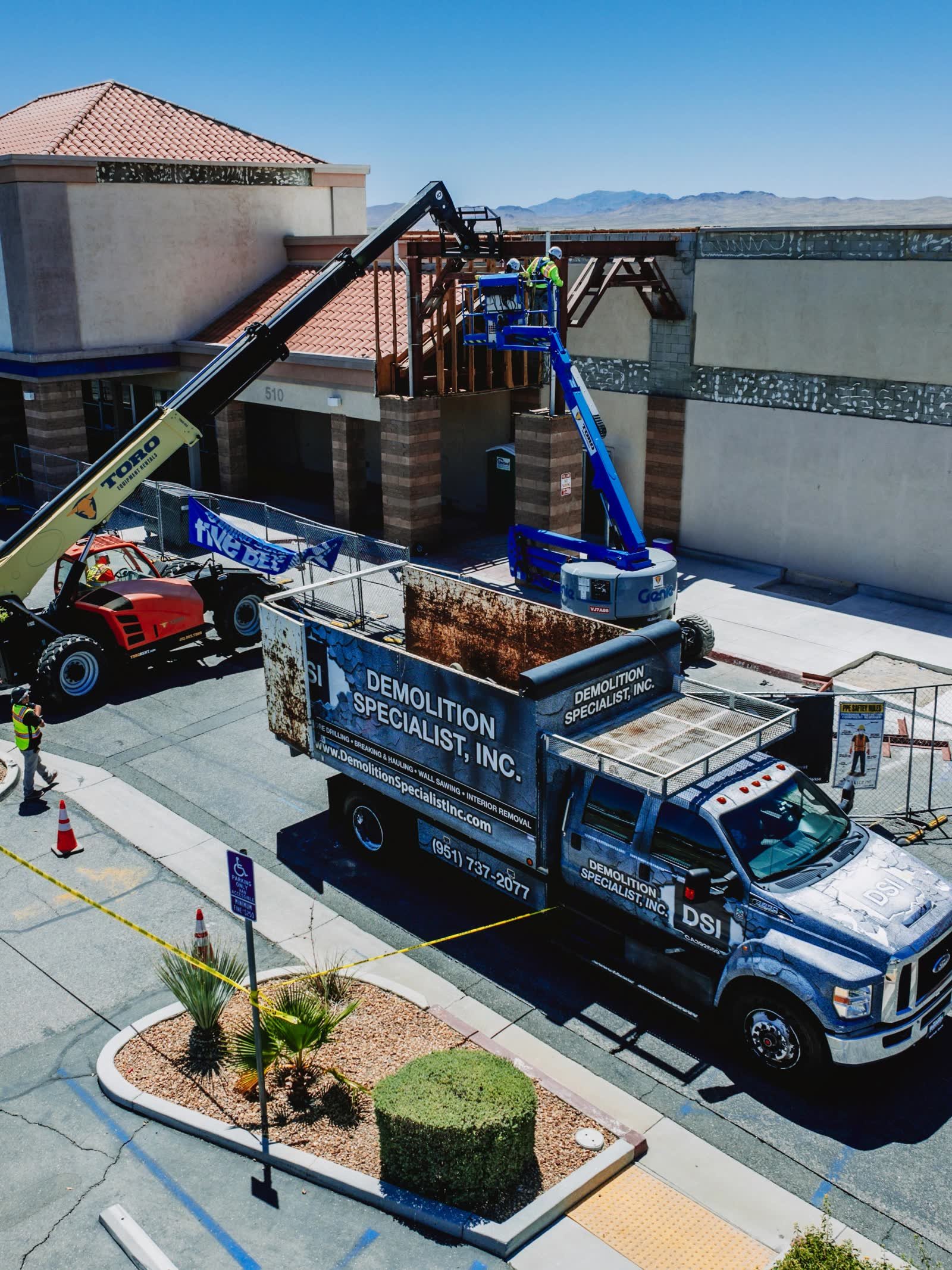Aerial view of DSI Demolition Specialist service truck parked with boom lift and crew working at elevation on commercial building