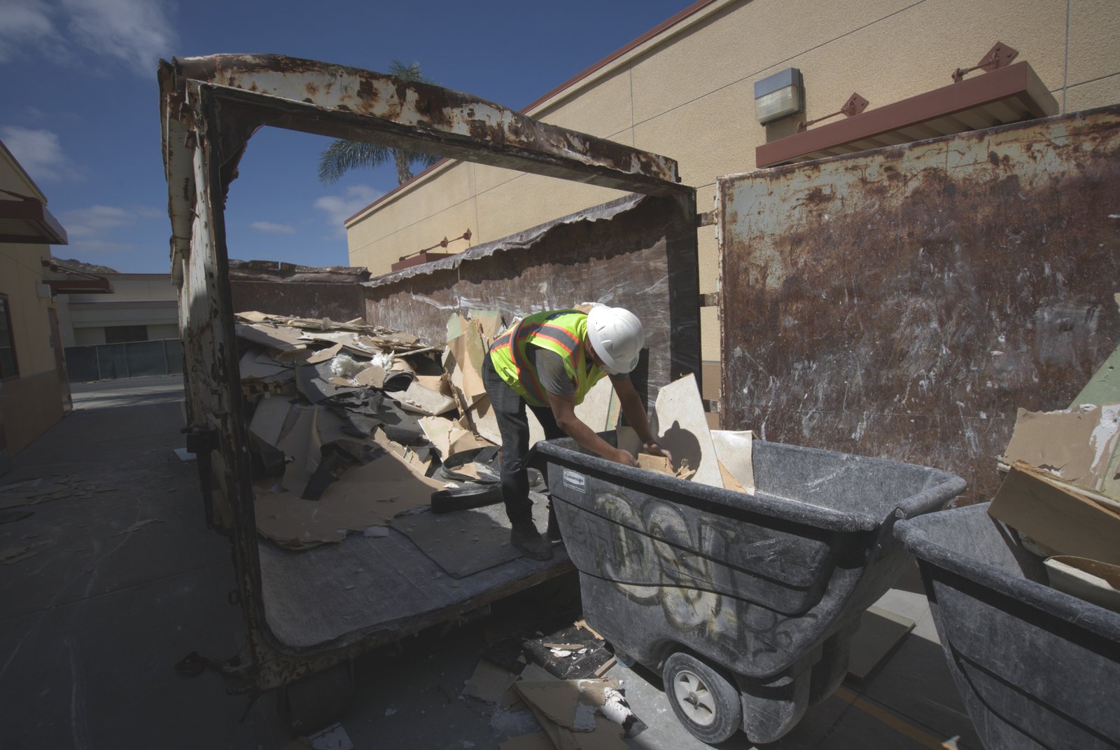 DSI crew member actively loading demolition debris into roll-off bin on commercial job site