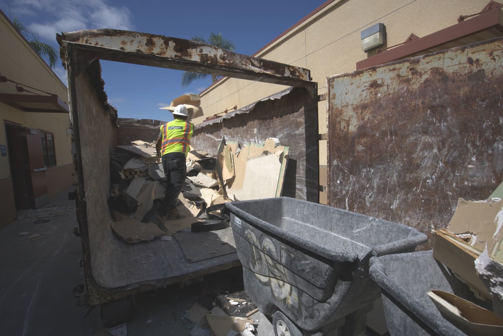 Worker standing inside roll-off bin organizing and loading construction demolition material