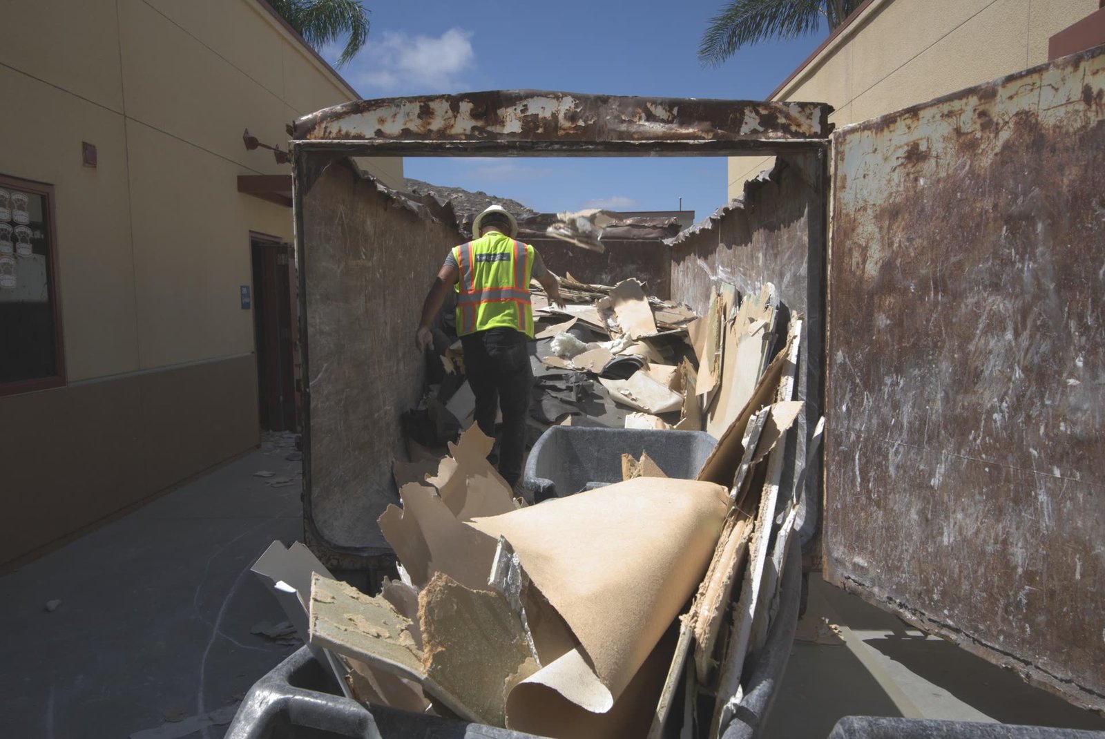 DSI laborer loading interior demolition debris into roll-off container from inside
