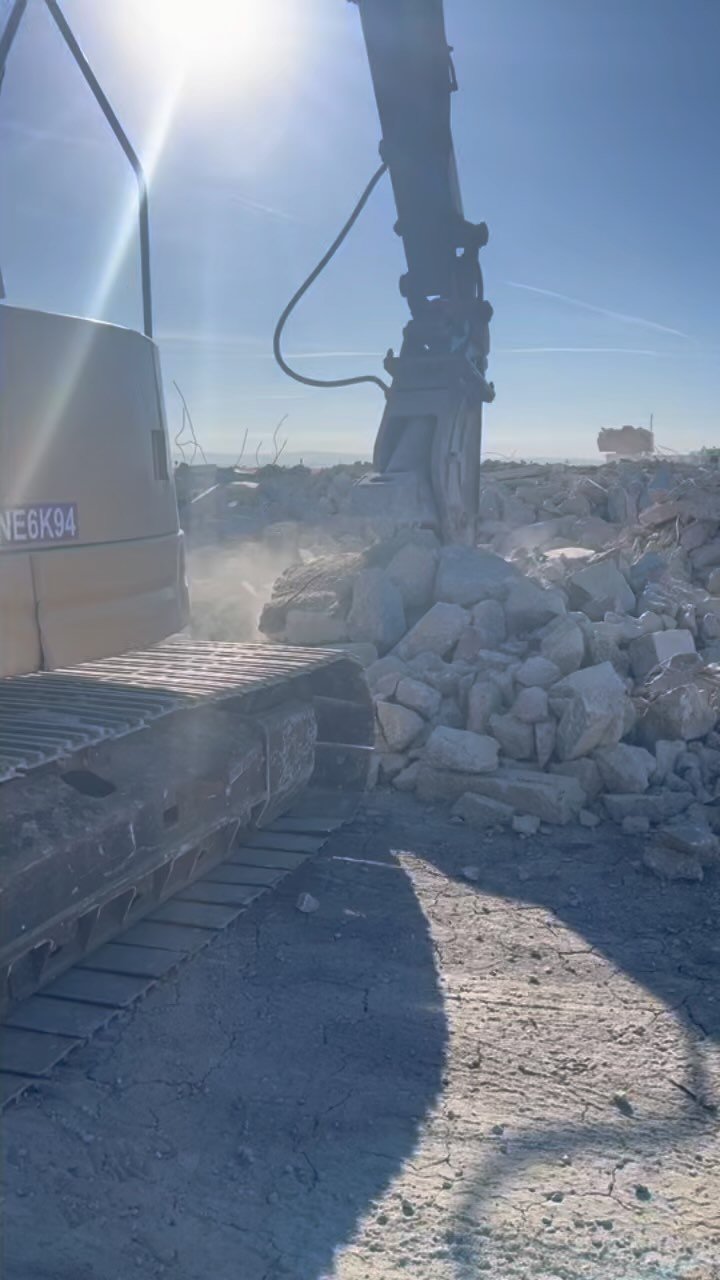 Excavator-mounted hydraulic breaker working through concrete debris pile on demolition site