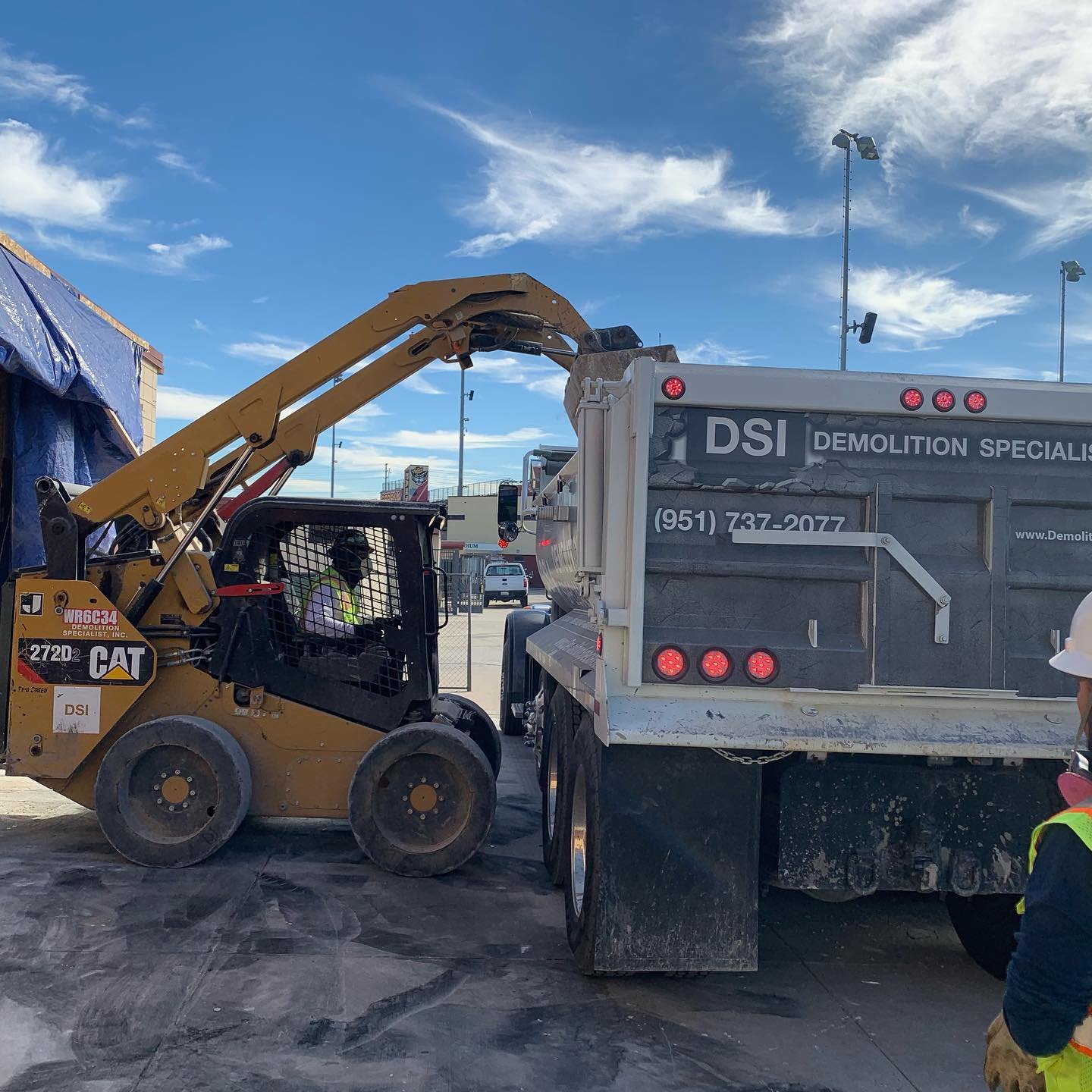 CAT skid steer loading debris into DSI Demolition Specialist dump truck on job site