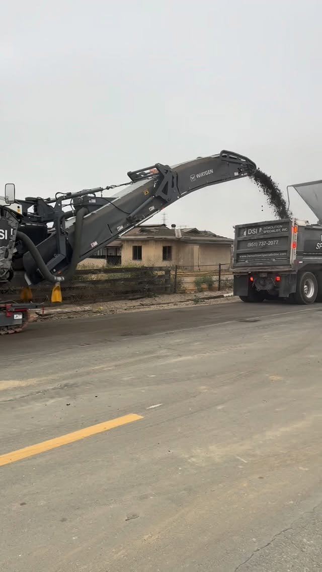 Wirtgen milling machine conveying material into DSI Demolition Specialist dump truck during road work