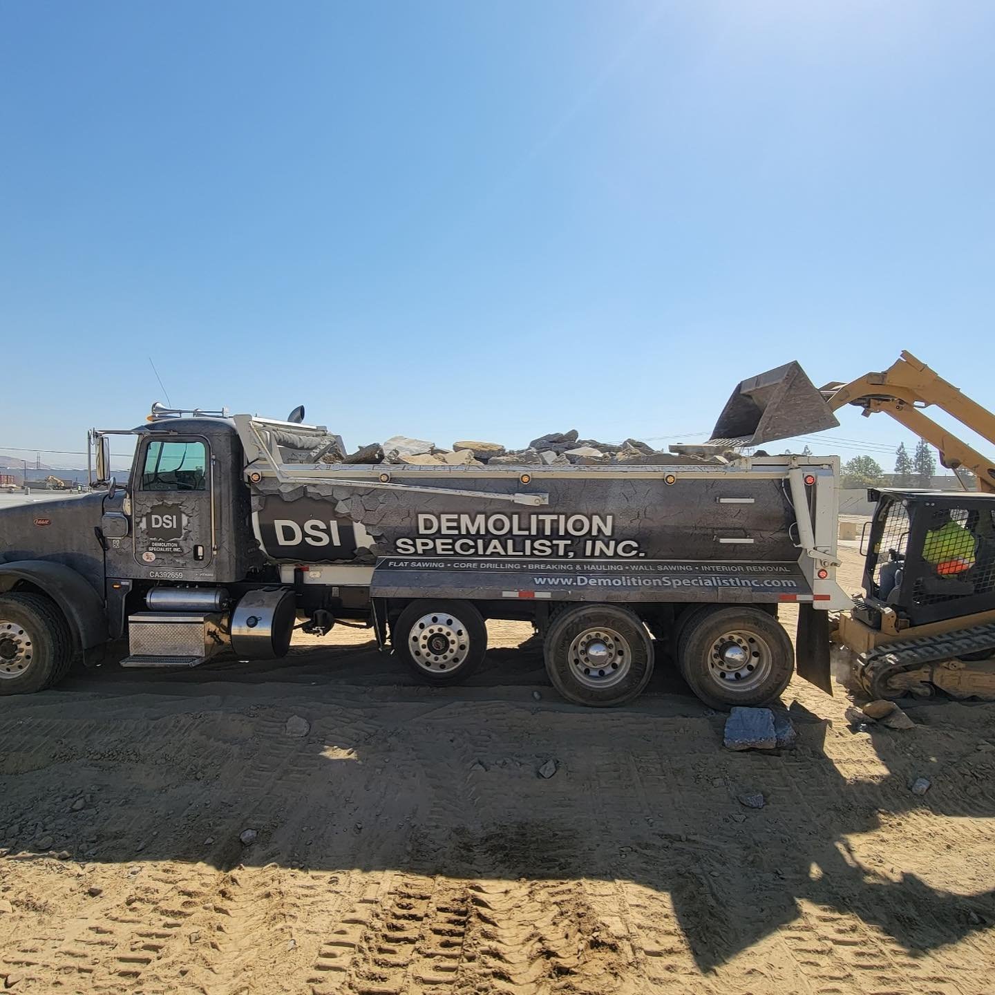DSI Demolition Specialist Peterbilt Super 10 dump truck being loaded by CAT excavator on active job site
