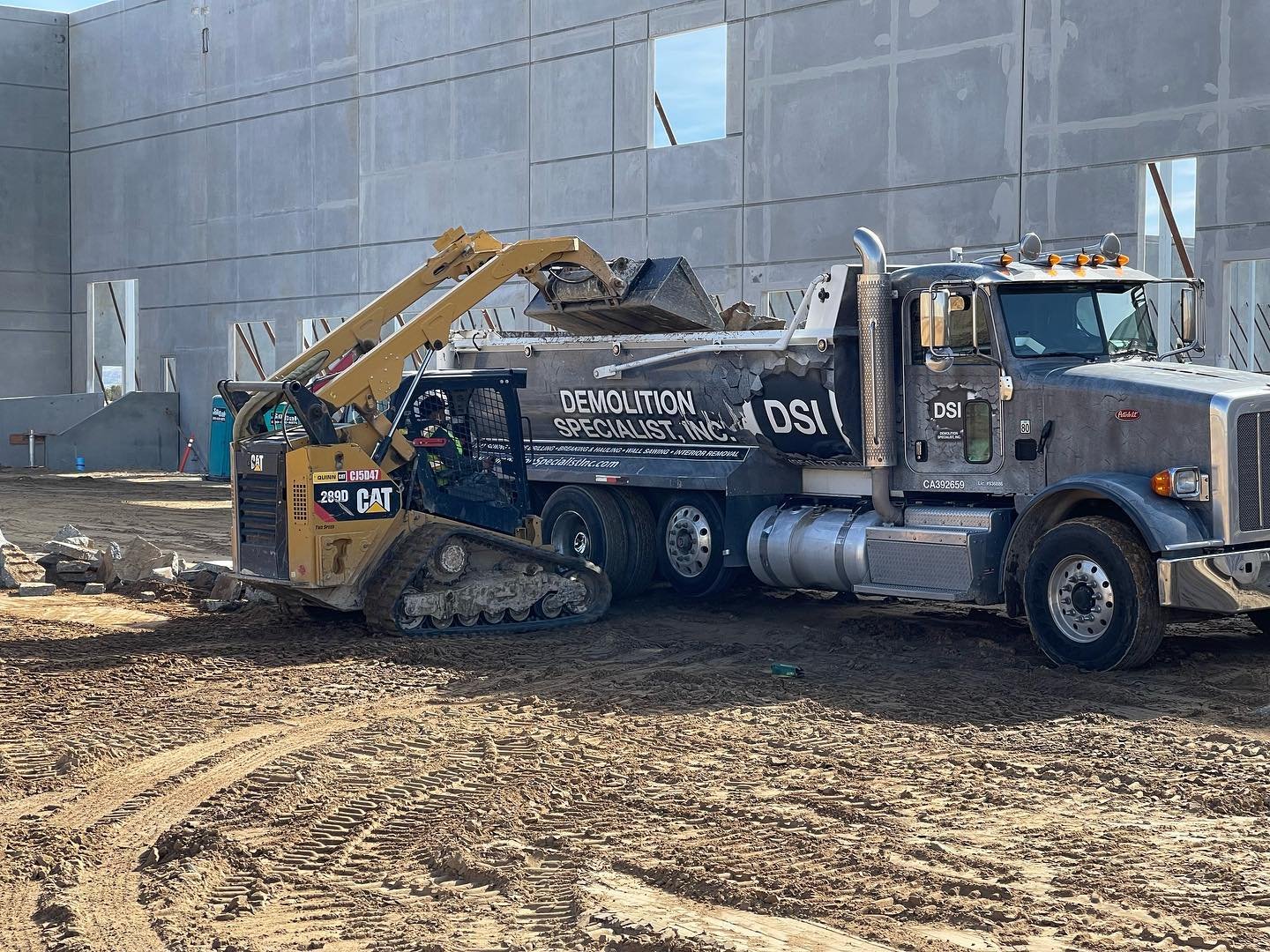 CAT track skid steer loading rubble into DSI Demolition Specialist dump truck at construction site
